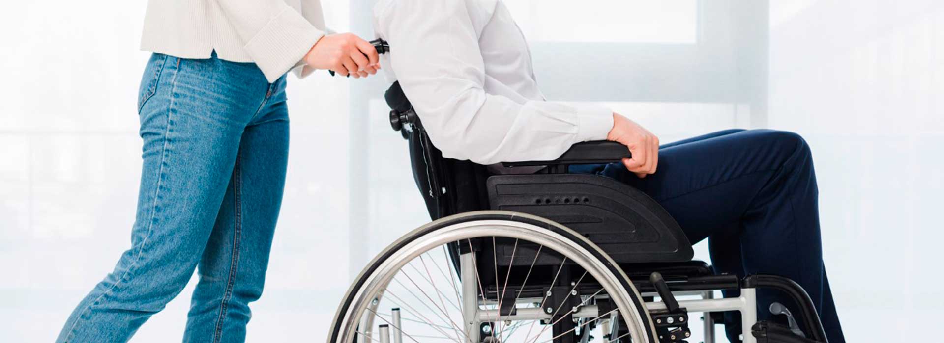 Imagen de persona con movilidad reducida sobre silla de ruedas empujada por cuidador.